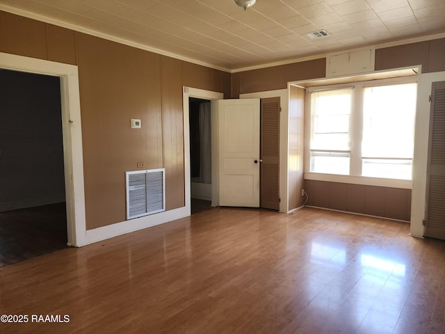 empty room with wood finished floors, visible vents, and crown molding