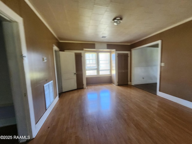 unfurnished bedroom featuring baseboards, visible vents, wood finished floors, and ornamental molding