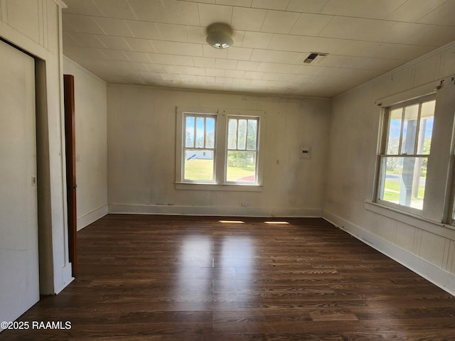 unfurnished room featuring a healthy amount of sunlight, visible vents, and dark wood-type flooring