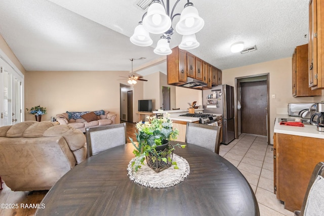 tiled dining area featuring ceiling fan with notable chandelier, a textured ceiling, and vaulted ceiling