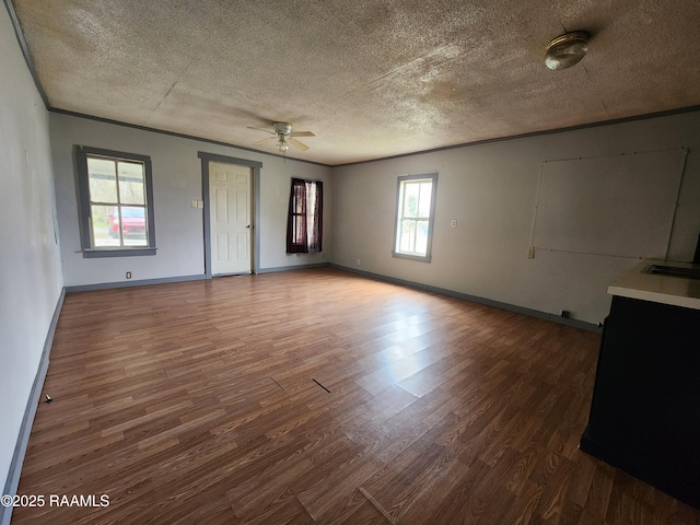 unfurnished living room featuring baseboards, a ceiling fan, ornamental molding, wood finished floors, and a textured ceiling