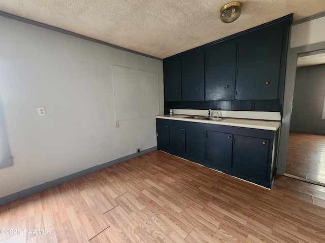 kitchen with baseboards, light countertops, a textured ceiling, and light wood finished floors