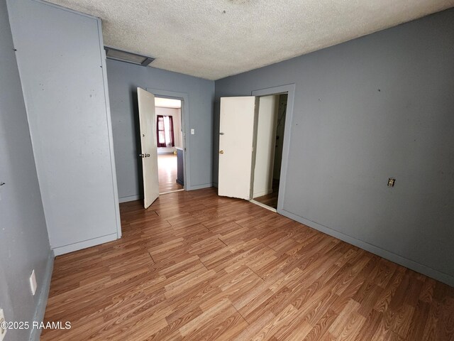 unfurnished room featuring a textured ceiling, light wood-type flooring, and baseboards