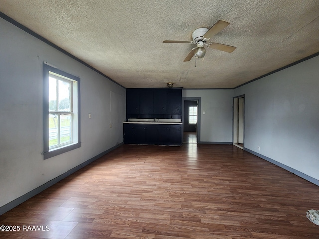 unfurnished living room featuring ceiling fan, a textured ceiling, baseboards, and wood finished floors