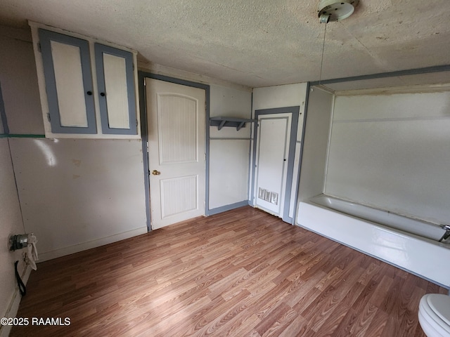 unfurnished bedroom featuring a textured ceiling, baseboards, and light wood-style floors