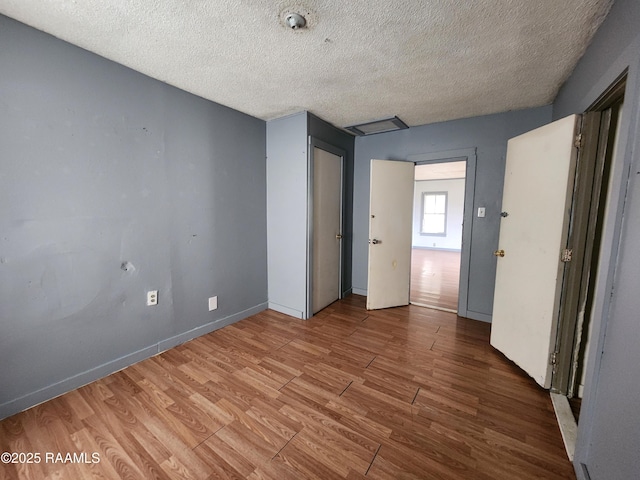 unfurnished bedroom with a closet, a textured ceiling, baseboards, and wood finished floors