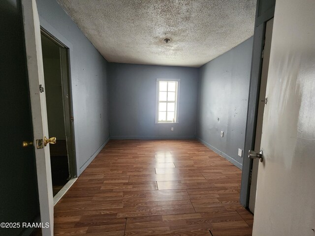 spare room with a textured ceiling, baseboards, and wood finished floors