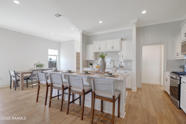 kitchen with light stone counters, a center island with sink, white cabinets, and stainless steel range with gas stovetop