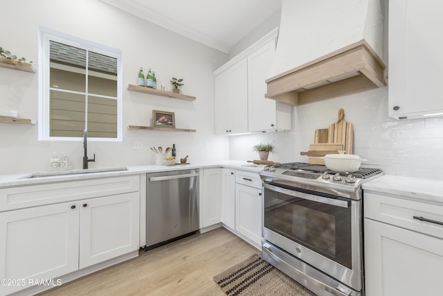 kitchen featuring custom exhaust hood, white cabinets, sink, light hardwood / wood-style flooring, and appliances with stainless steel finishes