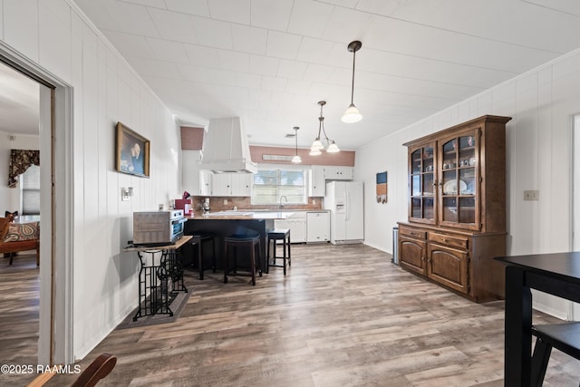 kitchen with premium range hood, white cabinetry, a kitchen breakfast bar, white appliances, and light wood-type flooring