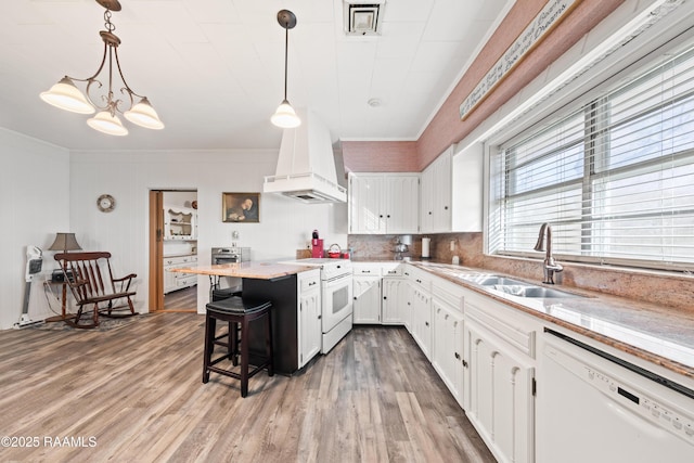 kitchen with pendant lighting, sink, white cabinets, custom range hood, and white appliances