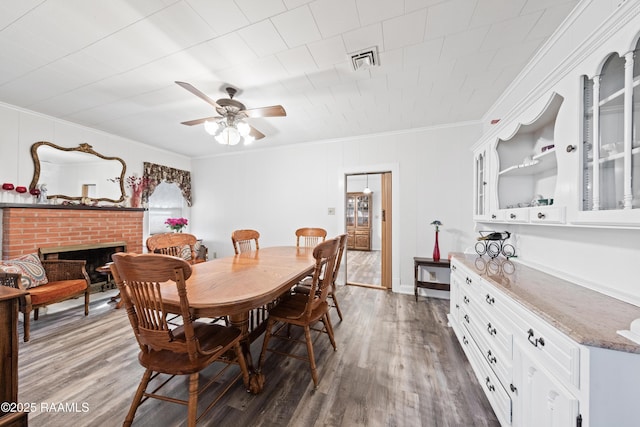 dining room with crown molding, ceiling fan, dark wood-type flooring, and a brick fireplace