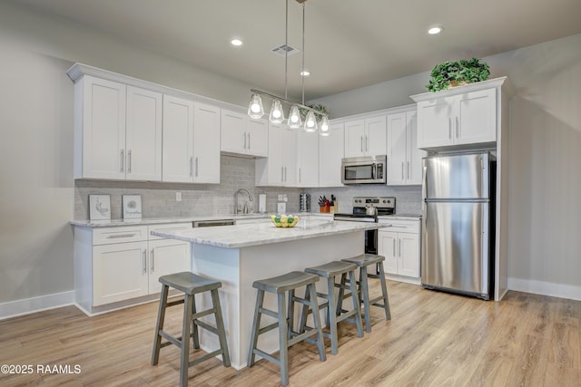 kitchen featuring white cabinetry, a center island, hanging light fixtures, and appliances with stainless steel finishes