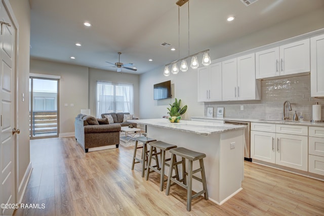 kitchen with decorative light fixtures, white cabinetry, a kitchen island, and sink