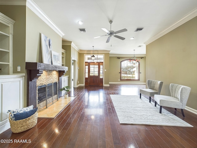 living room with dark hardwood / wood-style floors, built in features, crown molding, ceiling fan, and a premium fireplace