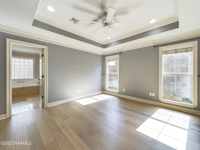 empty room featuring ceiling fan, crown molding, light wood-type flooring, and a tray ceiling