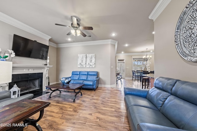 living room featuring ceiling fan with notable chandelier, a tile fireplace, crown molding, and hardwood / wood-style floors