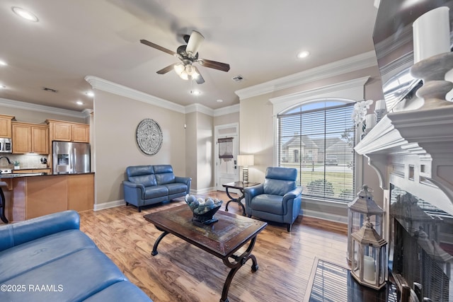 living room with light hardwood / wood-style floors, ceiling fan, a tiled fireplace, and crown molding