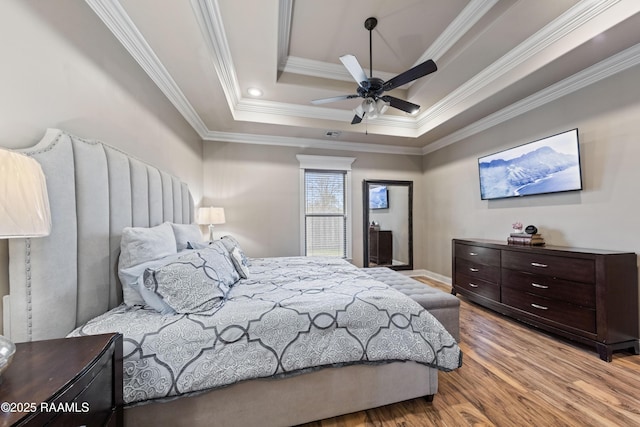 bedroom with ornamental molding, ceiling fan, a tray ceiling, and light hardwood / wood-style flooring