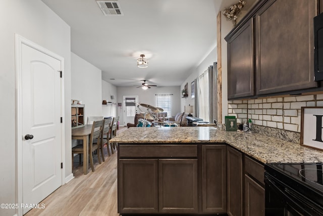 kitchen with kitchen peninsula, light stone countertops, ceiling fan, dark brown cabinetry, and light hardwood / wood-style flooring