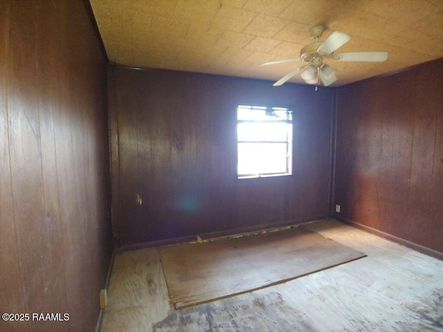 empty room with ceiling fan and wood walls