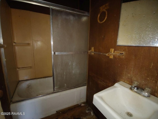 bathroom featuring sink, bath / shower combo with glass door, and wooden walls