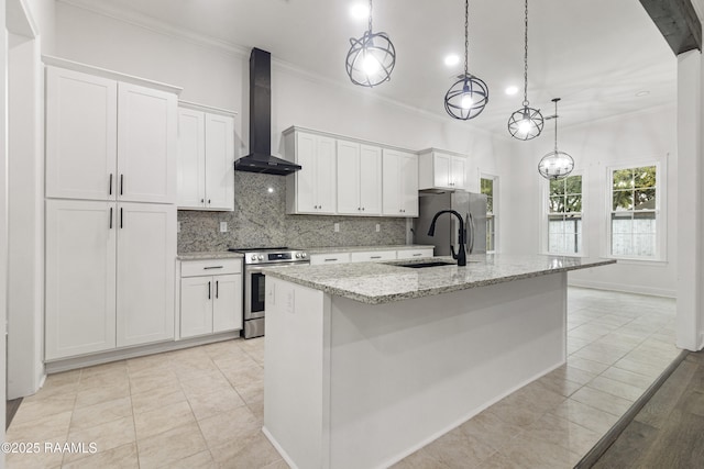 kitchen with appliances with stainless steel finishes, wall chimney exhaust hood, pendant lighting, white cabinetry, and an island with sink