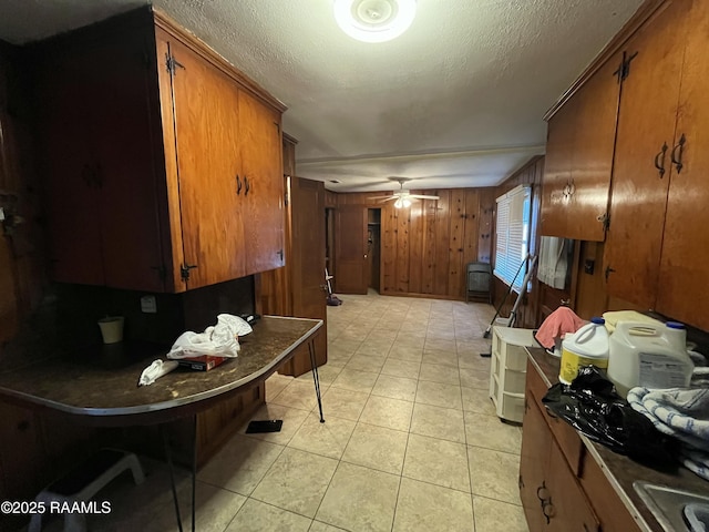 kitchen featuring ceiling fan, wooden walls, a textured ceiling, and light tile patterned floors