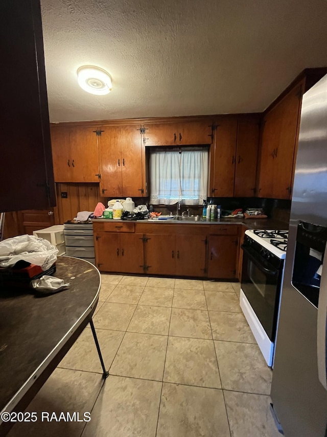 kitchen with sink, range with gas stovetop, a textured ceiling, light tile patterned flooring, and stainless steel fridge with ice dispenser