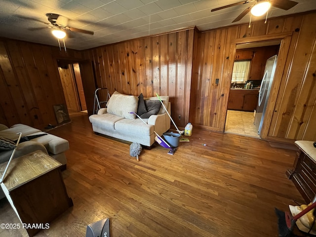 living room with wood-type flooring, ceiling fan, and wood walls