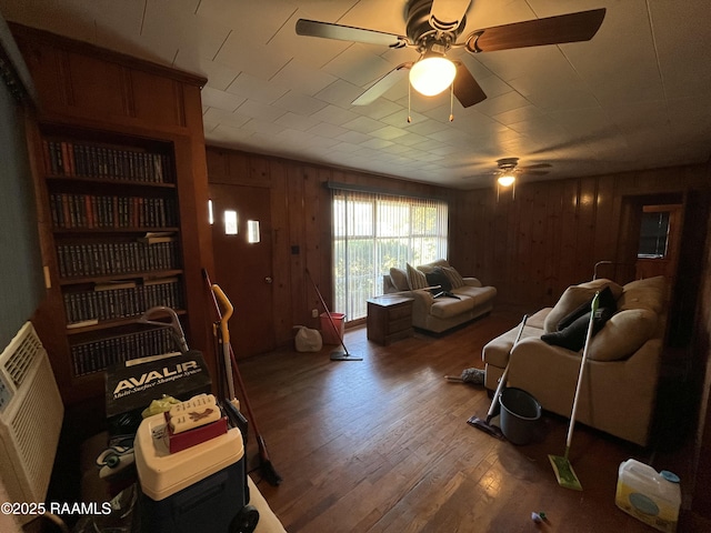 living room with wood-type flooring, ceiling fan, and wood walls