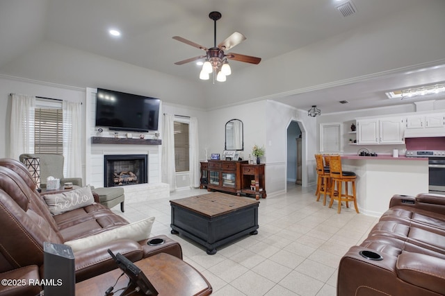 living room with a raised ceiling, light tile patterned flooring, a large fireplace, and ceiling fan