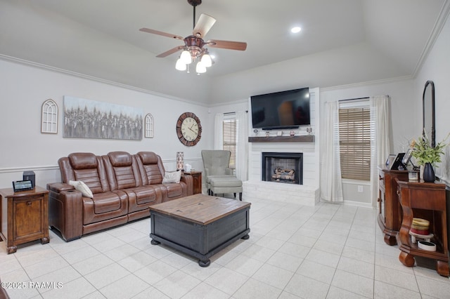 tiled living room with ceiling fan, a large fireplace, a tray ceiling, and crown molding