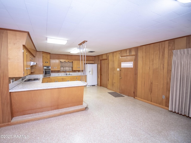 kitchen featuring kitchen peninsula, wooden walls, stainless steel appliances, pendant lighting, and sink