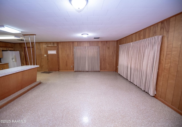 interior space with white fridge with ice dispenser and wooden walls