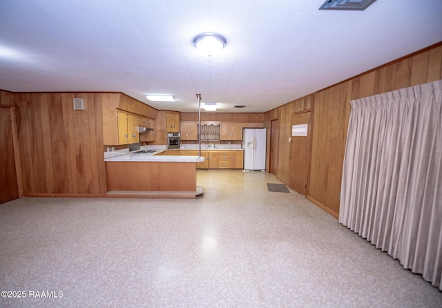 kitchen featuring kitchen peninsula, wooden walls, gas cooktop, stainless steel oven, and white fridge with ice dispenser