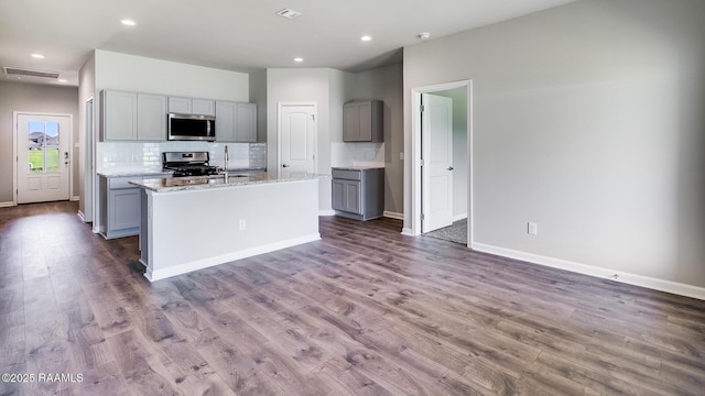 kitchen featuring gray cabinetry, backsplash, dark wood-type flooring, an island with sink, and appliances with stainless steel finishes