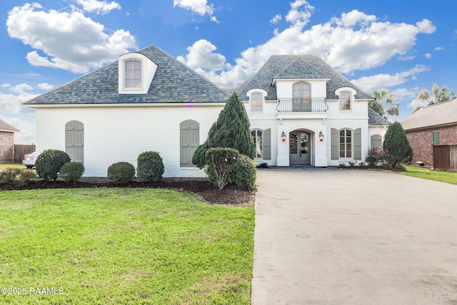 french country home featuring a balcony and a front lawn