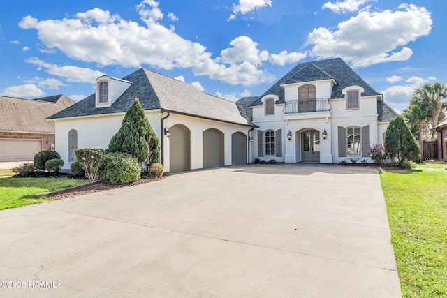 french country home with a balcony, a front lawn, and a garage