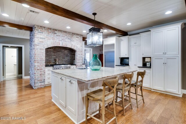 kitchen with pendant lighting, light stone countertops, a center island with sink, and white cabinets