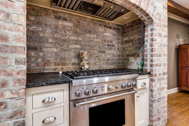 kitchen with wall chimney range hood, stainless steel gas range oven, and brick wall