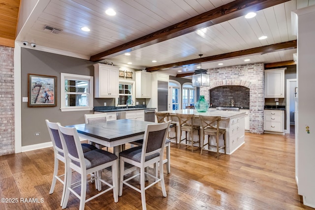 dining area with beamed ceiling, brick wall, sink, and light hardwood / wood-style floors