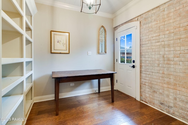 foyer entrance with hardwood / wood-style floors, ornamental molding, a chandelier, and brick wall