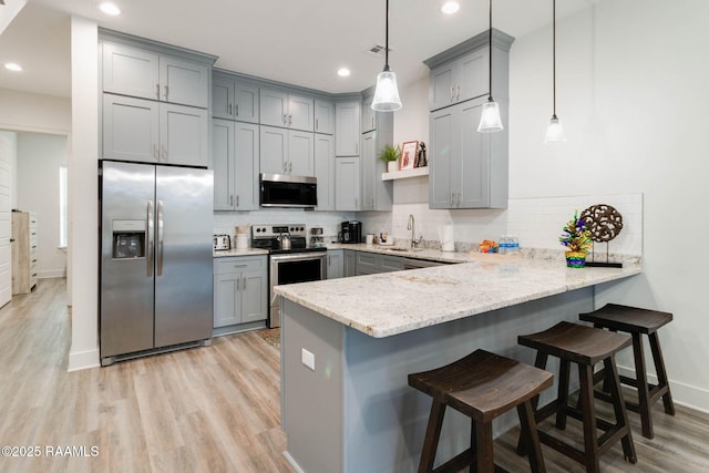 kitchen with a kitchen breakfast bar, tasteful backsplash, kitchen peninsula, pendant lighting, and appliances with stainless steel finishes