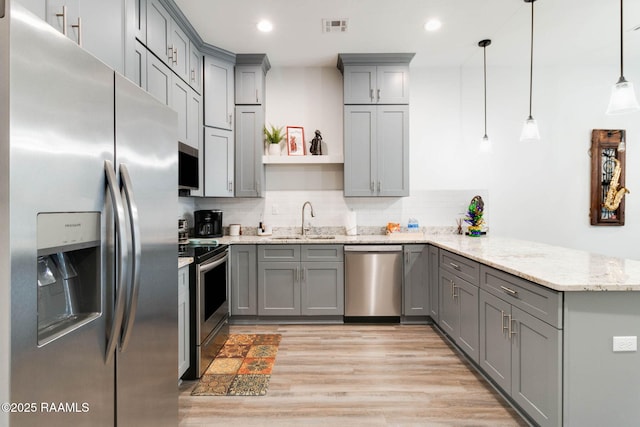 kitchen featuring pendant lighting, gray cabinets, appliances with stainless steel finishes, light stone counters, and kitchen peninsula