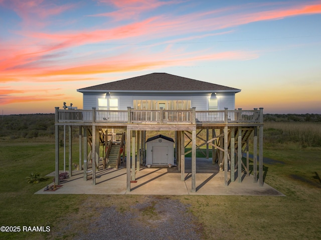 back house at dusk with a shed, a patio area, a lawn, and a deck