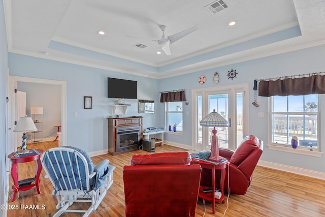 living room with ornamental molding, light hardwood / wood-style floors, and a raised ceiling