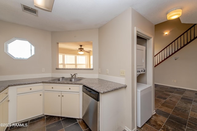 kitchen with ceiling fan, stainless steel dishwasher, sink, stacked washer and clothes dryer, and white cabinets