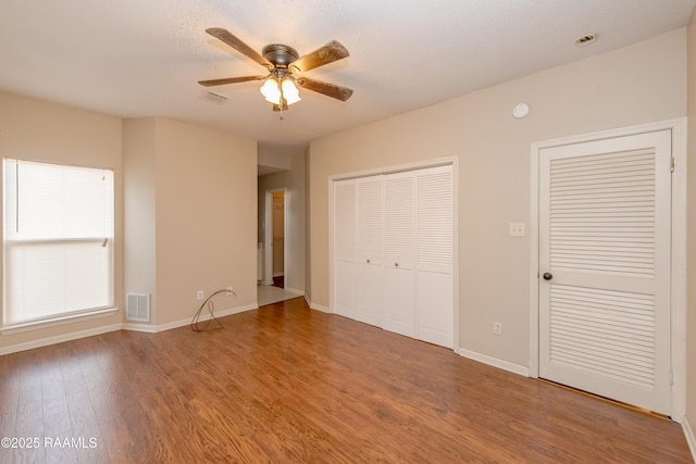 unfurnished bedroom featuring ceiling fan, two closets, and hardwood / wood-style floors