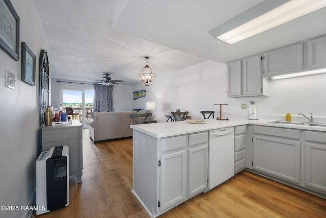 kitchen featuring dishwasher, sink, hanging light fixtures, kitchen peninsula, and light hardwood / wood-style flooring